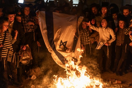 Orthodox Jews gather around an Israeli flag burning.