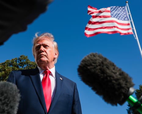 Man in suit with microphones in foreground and US flag above.