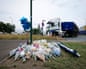 Flowers arranged by roadside with a blue balloon and a blue and white lorry in background.