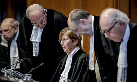 Woman wearing glasses and black judge robe sits in front of microphone as men wearing glasses and black judge robes sit down around her.