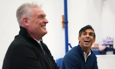 Lee Anderson, slightly out of focus in the foreground, sitting next to Rishi Sunak, in focus in the background, laughing
