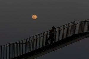 A man and child walk on a bridge with a rising pink supermoon in the background, as the outbreak of Covid-19 continues in Karachi, Pakistan.