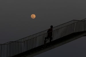 A man and child walk on a bridge with a rising pink supermoon in the background, as the outbreak of Covid-19 continues in Karachi, Pakistan.