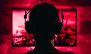 a woman wearing headphones plays a video game in a red-light saturated room