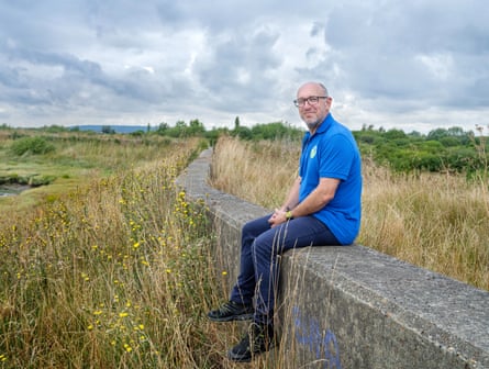 Man sits on a long concrete slab surrounded by long grasses.