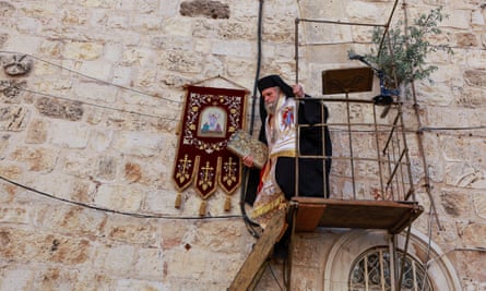 A cleric climbs down from a rickety pulpit built against a stone wall