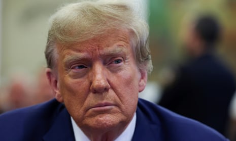 Donald Trump, wearing a blue suit, sits in a court room and looks to the side