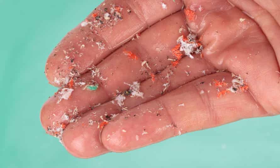 Detalles de la mano que muestran microplásticos sobre el agua 
