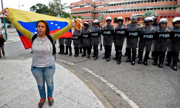 A woman waves a Venezuelan flag in front of a line of riot police outside the Venezuelan navy command headquarters in the San Bernardino neighborhood in Caracas on 4 May.