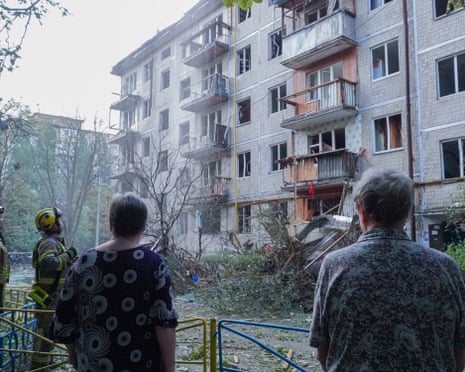 Firefighters and residents stand outside a charred and damaged building