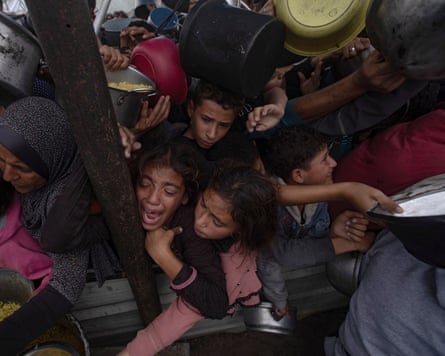 Palestinians, including children, holding metal pots and pans, gather to receive food cooked by a charity kitchen, in Khan Younis, southern Gaza.