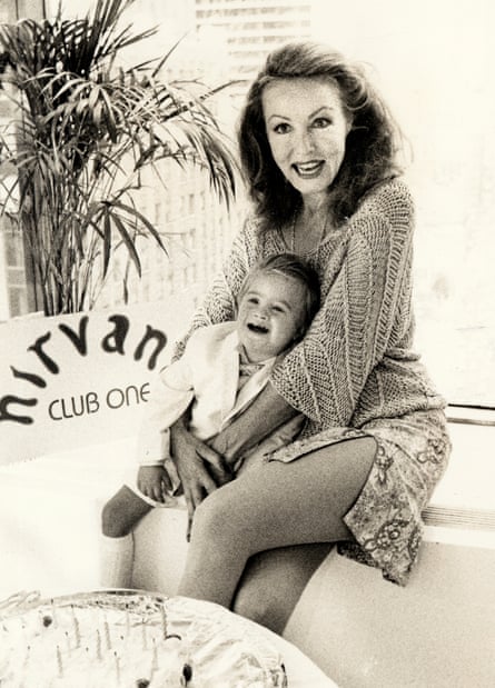A woman sits smiling with her baby son on her lap.