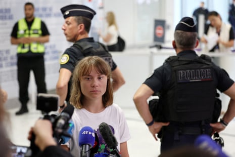 Swedish activist Greta Thunberg talks to journalists surrounded by French police as she arrives at a terminal at the Paris-Charles de Gaulle Airport.