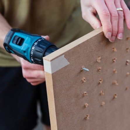 A close up of the Makita cordless drilling a grid of holes through a sheet of MDF. The writers hands are in view holding the sheet of wood.
