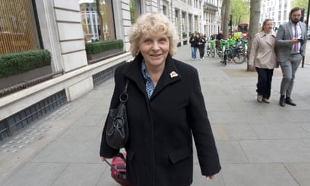 Jo Hamilton smiling, photographed walking along the street pulling a small wheelie case