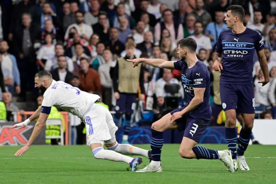 „Manchester City“ žaidėjas Rubenas Diasas (centras) prasižengia prieš Madrido „Real“ žaidėją Karimą Benzema, o teisėjas rodo tašką.