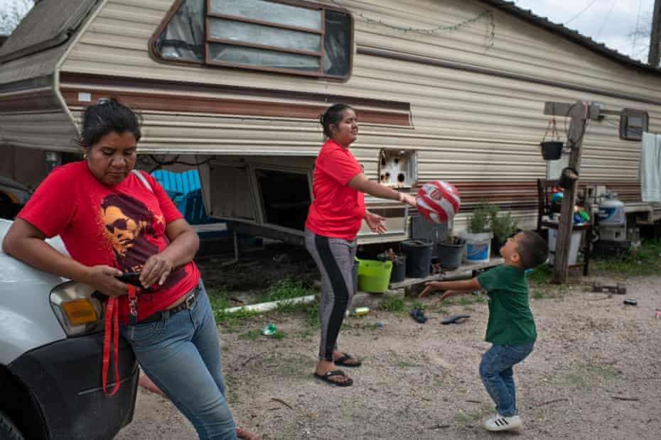 Irene returns from working in the fields, while her daughter, Kori, plays with her son in front of their house.