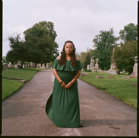 a woman standing at a cemetery wearing a green dress