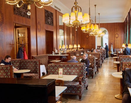 Interior of cafe with wood-panelled and mirrored walls, chandeliers and banquette seating