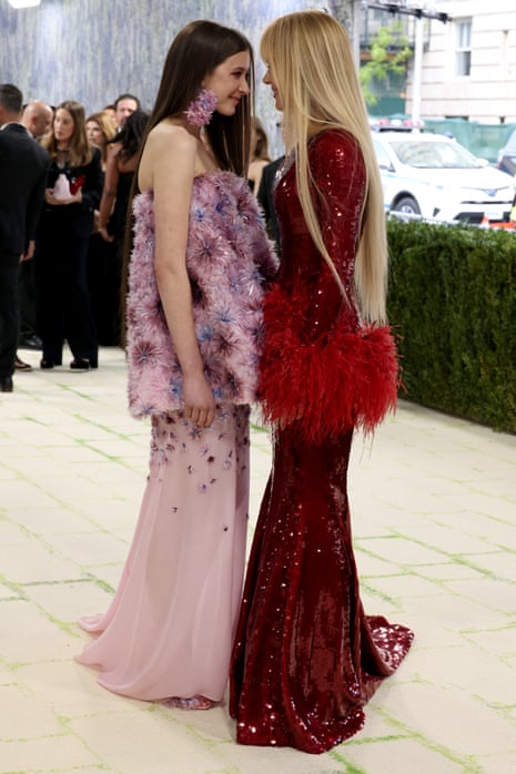 woman in pink dress and woman in red dress stand close together, facing each other