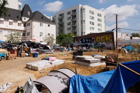 An empty lot beside nice white buildings with many mattresses and tents on the ground.