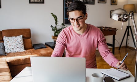 A young man with a laptop at home, he is working and writing notes in a notebook