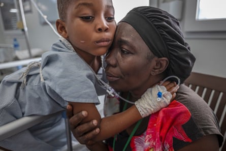 A boy with a drip in his hand puts his arms around a woman