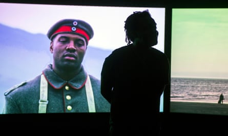 Akomfrah in front of an image of a Black soldier in uniform.