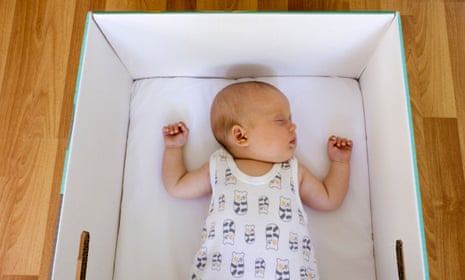 Young baby is sleeping in a Finnish maternity box that can be used as a first crib. 