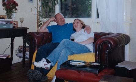Foster sits with Barrie Jackson on a Chesterfield sofa in a sitting room. He has his arm around her, she is holding a glass of red wine. They are both laughing.