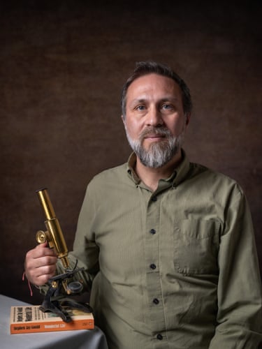 A man holds a microscope that rests on a book