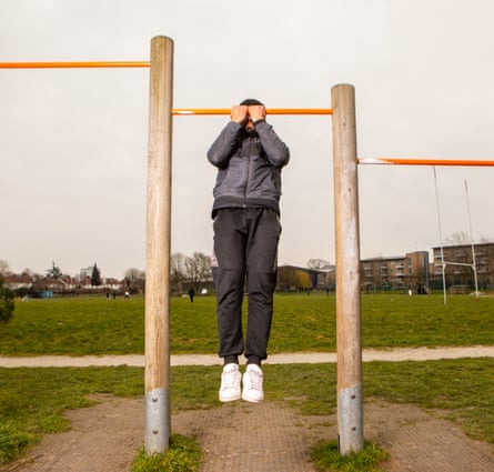 Arkan, a Kurdish asylum seeker from Iran, doing a pull-up in an outside gym, with his face obscured by the bar and his hands