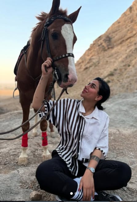 Taraneh Rahimi sitting on the ground patting the face of a horse