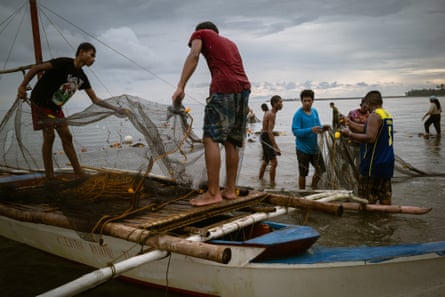 Men stand on boats and in shallow water holding fishing nets