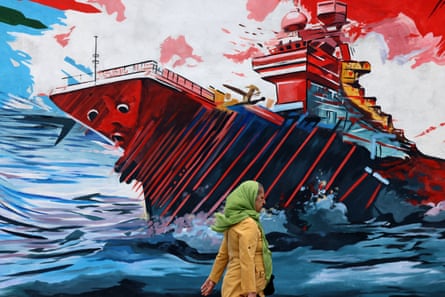 A woman in a headscarf walks past a mural depicting a warship