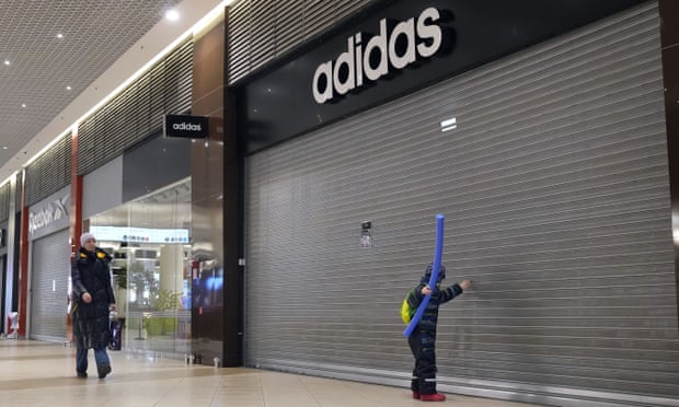 İnsanlar St. Petersburg'daki bir alışveriş merkezinde kapalı Adidas, Reebok ve diğer mağazaların yanından geçiyor