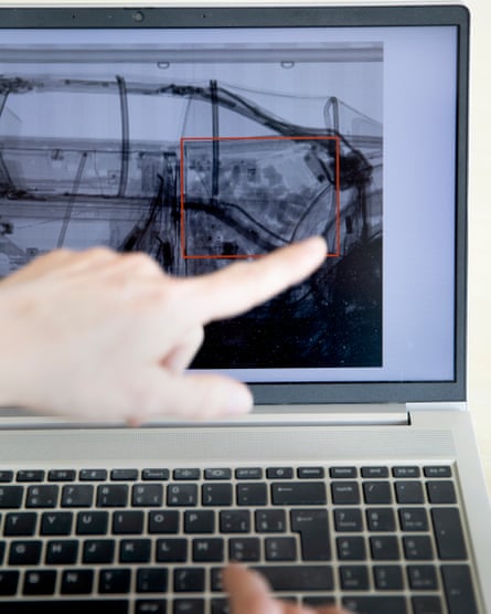 A hand pointing at a screen showing a scan of a car, with an area highlighted by a red box