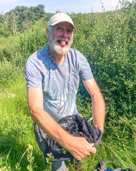 Dr David Wainwright in a pale baseball cap and palm motif T-shirt holds a butterfly net while among greenery