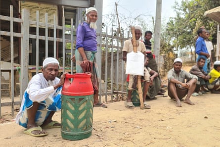 A man crouches beside a gas canister on a dusty street. Several other people stand around nearby
