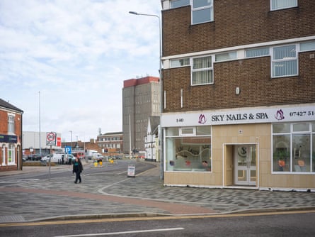 A person crosses a road next to a nail bar on an otherwise deserted street