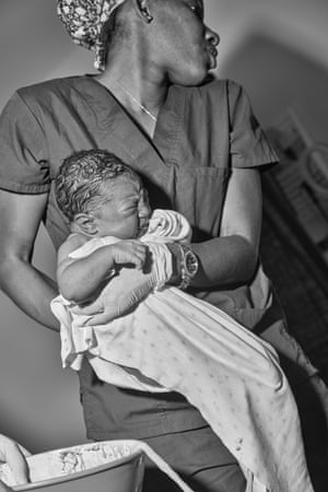 Jezreel De Cohen, a student midwife and doula, holds Aquilla’s daughter Storie as Aquilla gets settled into a bed after her labour at New Life Midwifery Birth Center.