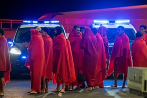 People wrapped in red blankets stand in a line