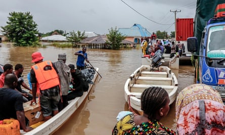 People sit in boats on muddy water with submerged buildings in the background