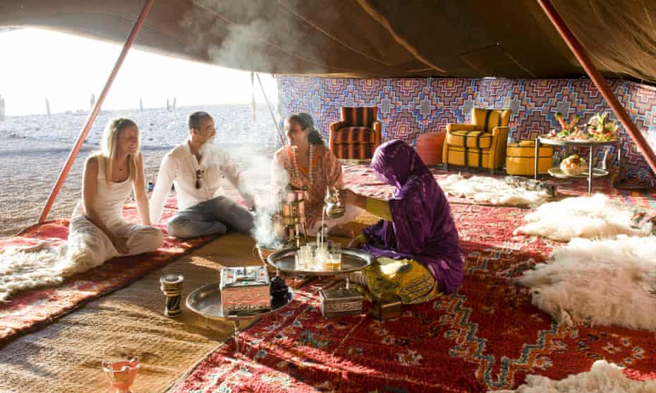 A group of people sitting on Moroccan rugs in a tented area on the beach