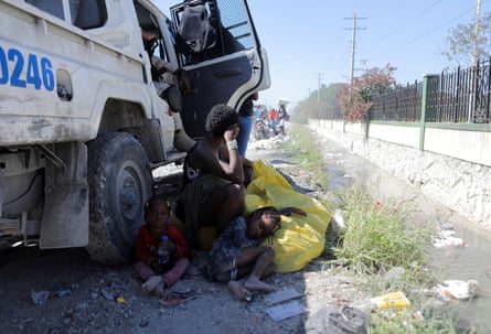 A woman and two children displaced by gang violence shelter next to a police truck in Port-au-Prince.