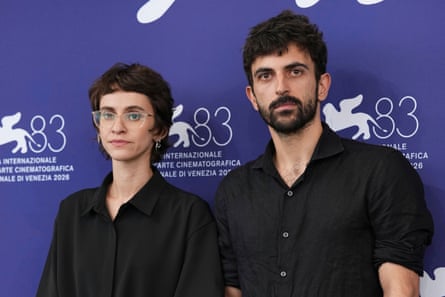Rachel Szor and Yuval Abraham, both dressed in black, stand in front of a Venice film festival media wall
