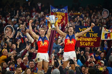 Oscar Allen and Sam Draper lift the premiership cup with Lions fans at the MCG.