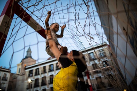 A woman in a football shirt lifts her baby son up to the goal net above them