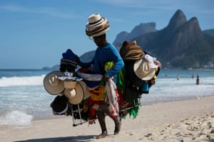 A vendor walks with his hats and beachwear on a beach