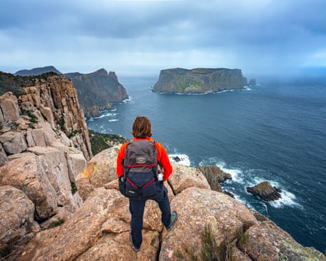 A woman looks out at the ocean from a clifftop on the Three Capes Walk in Tasmania, Australia